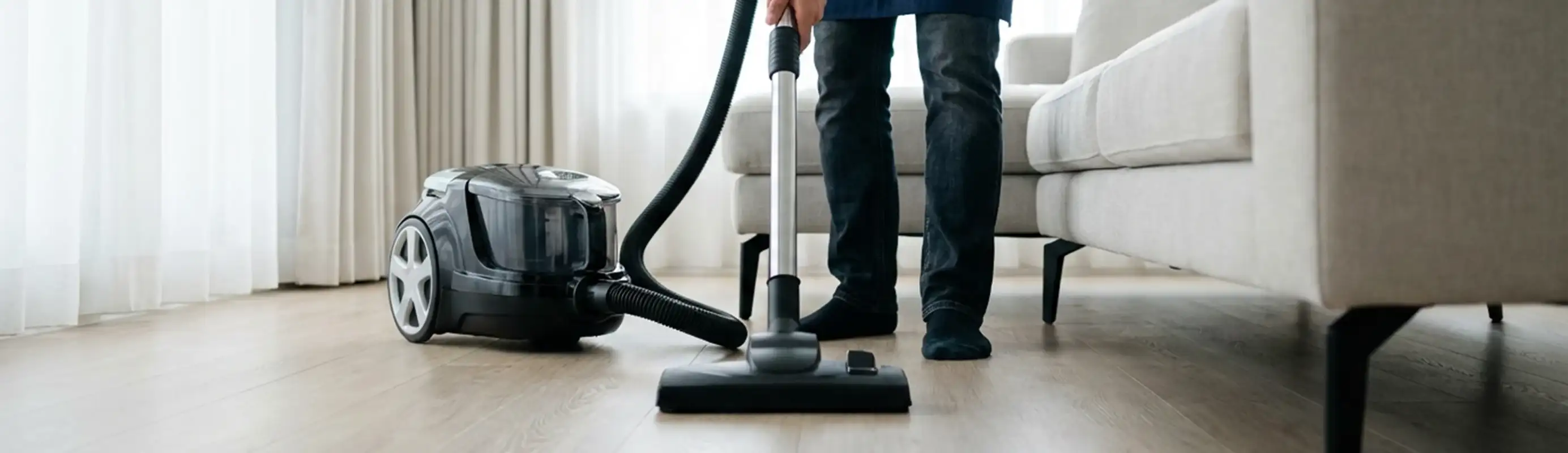 Professional house cleaner vacuuming a living room floor with a canister vacuum cleaner, Saint Louis, MO.