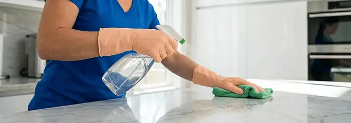 Maid service worker spraying and wiping a kitchen countertop with a microfiber cloth for sanitizing, Saint Louis, MO.
