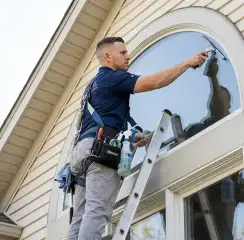 Professional window cleaner on a ladder using a squeegee to clean an exterior arched window, Saint Louis, MO.
