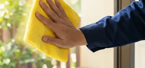 House cleaner wiping a glass window with a yellow microfiber cloth for streak-free cleaning, Saint Louis, MO.